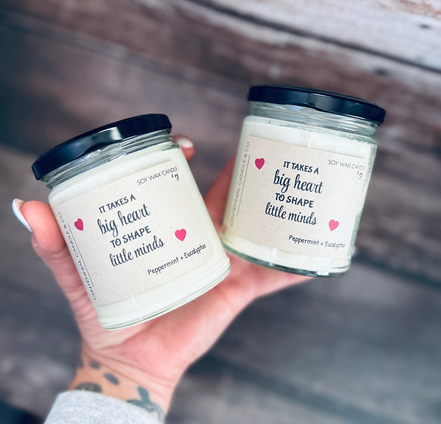 a person holding two jars of white candles