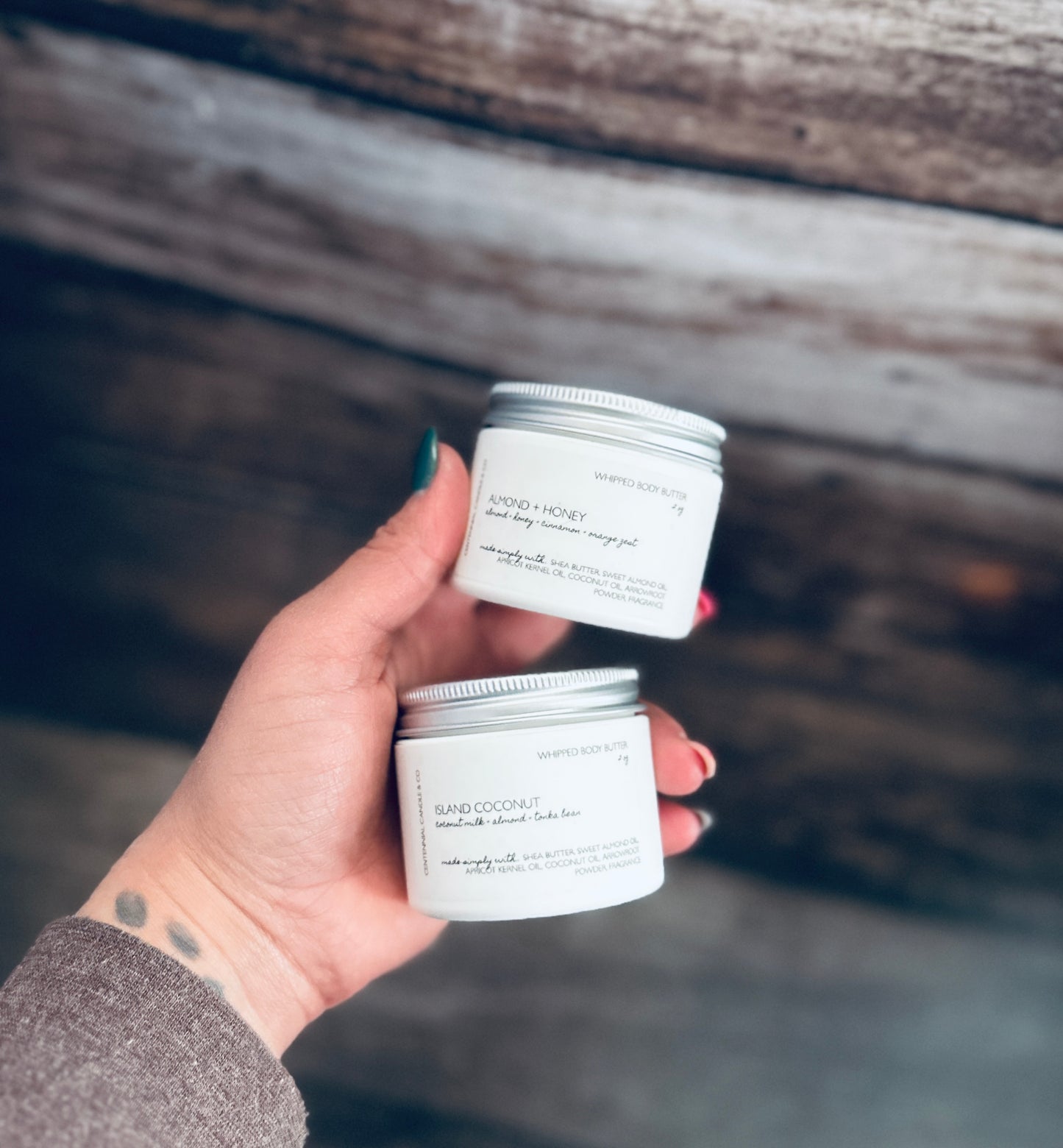 a person holding two jars of body butter